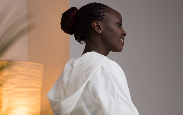 Woman in a white robe smiling in a peaceful spa setting.