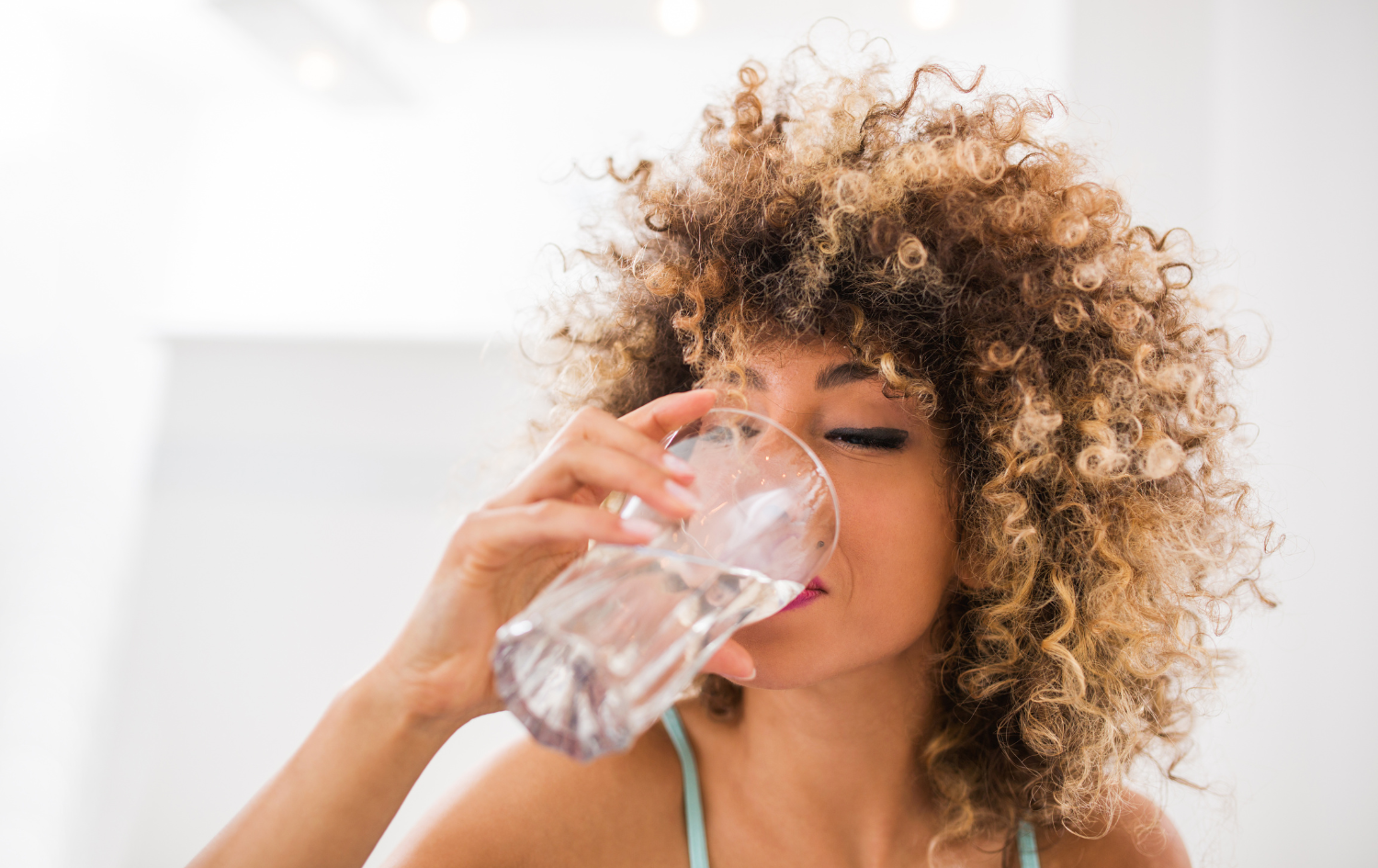 Woman with curly hair drinking a glass of water.