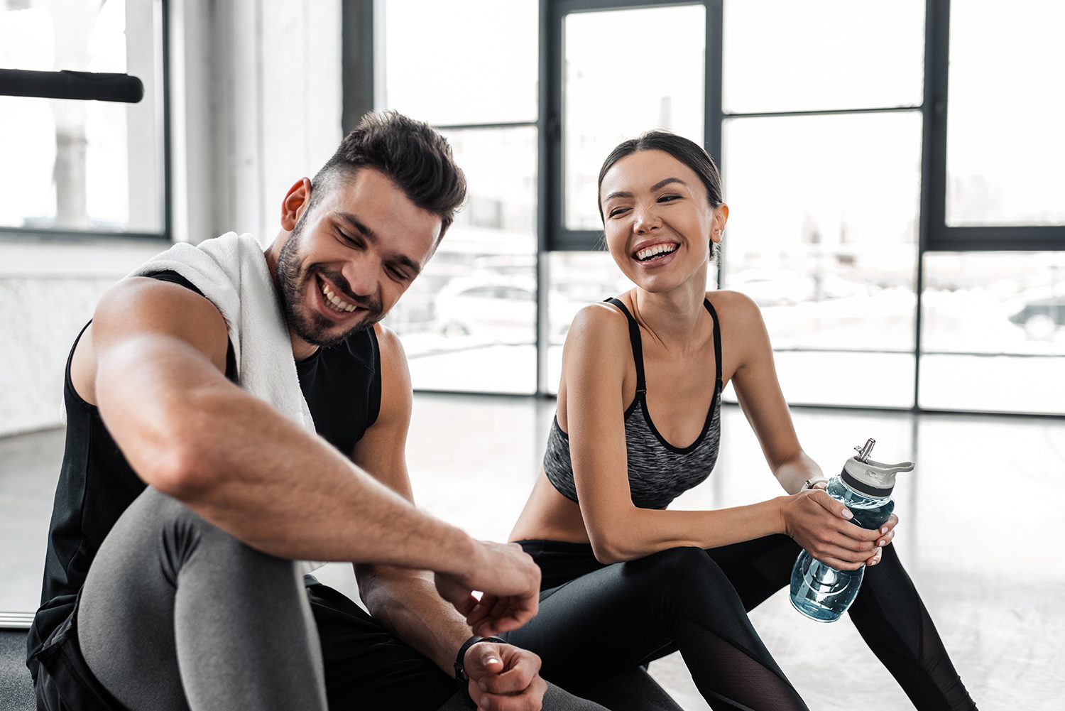 Smiling man and woman resting after workout in gym